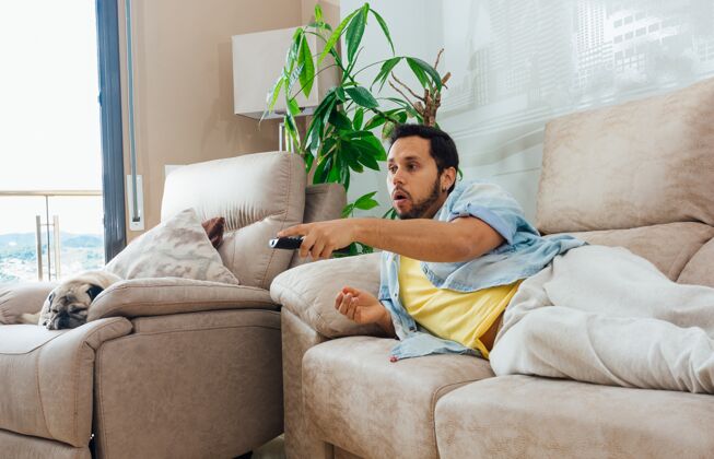 放松一位英俊的西班牙裔男子躺在沙发上看电视的照片居住自信沙发