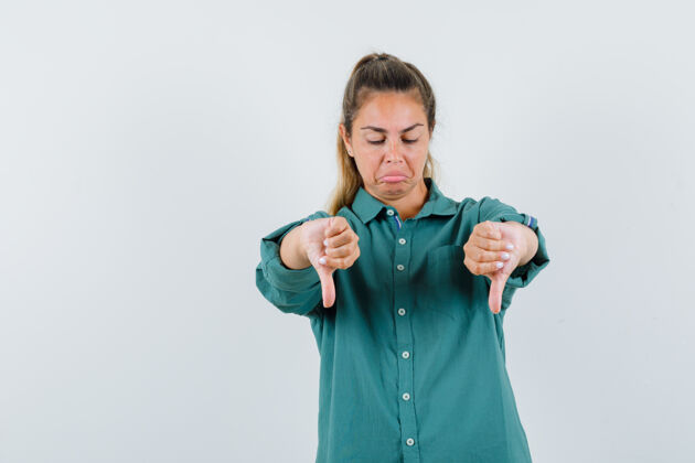 模型一个年轻的女人双手竖起大拇指 穿着绿色的衬衫做鬼脸 看起来很悲伤手肖像人