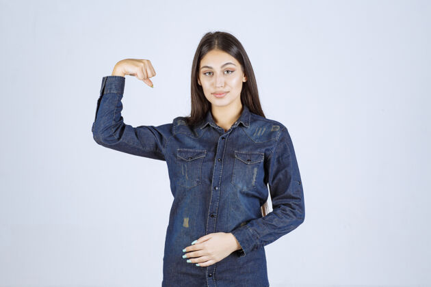 女人穿着牛仔衬衫的年轻女子展示了她的手臂肌肉拳头人运动