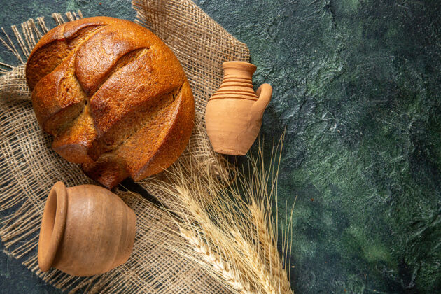 视图一条棕色毛巾上的黑面包和深色背景上右侧的陶器的俯视图背景面包食物