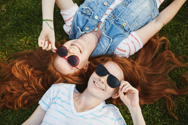 关系可爱无忧无虑的满脸雀斑的红发女同胞的画像 躺在公园的草地上 戴着时髦的太阳镜 边笑边谈云的形状Carefree身份情感