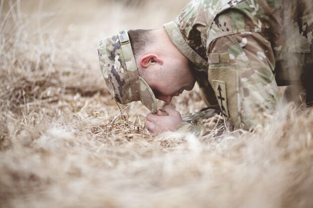 模糊浅焦拍摄一名美国士兵跪在干燥的草地上祈祷指导士兵战争