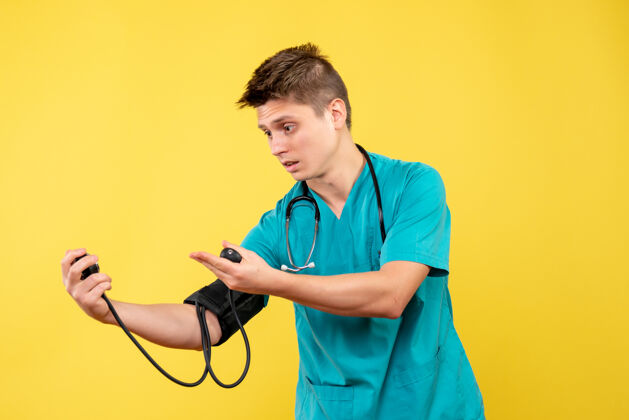 男医生穿着医疗服的男医生在黄色墙壁上检查压力的前视图套装检查医疗仪器