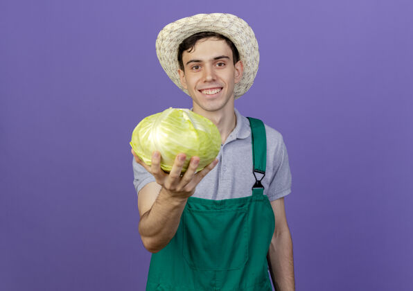 穿微笑的年轻男园丁戴着园艺帽捧着卷心菜帽子持有花园