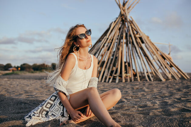 享受优雅的女人戴着黑色太阳镜坐在沙滩上看天空比基尼天空阳光