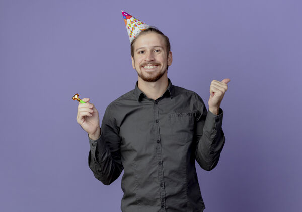 帅气戴着生日帽的微笑帅哥在紫色的墙上孤立地举着哨子和大拇指男人抱着拇指