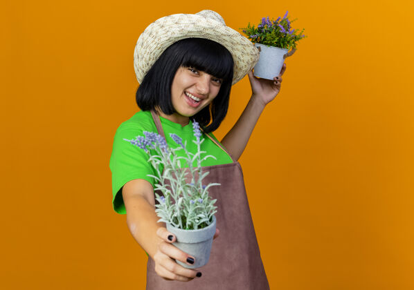 欢乐快乐的年轻女园丁穿着制服戴着园艺帽拿着花盆园艺举行制服