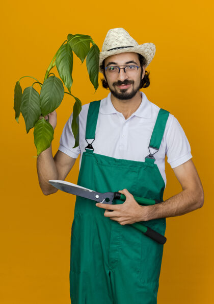 园艺高兴的男园丁戴着眼镜戴着园艺帽拿着植物和剪子空间复制眼镜