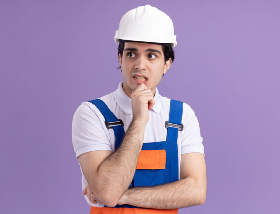 建设者身穿施工制服 头戴安全帽的年轻建筑工人站在紫色的墙上 一边沉思一边思考沉思男人建筑