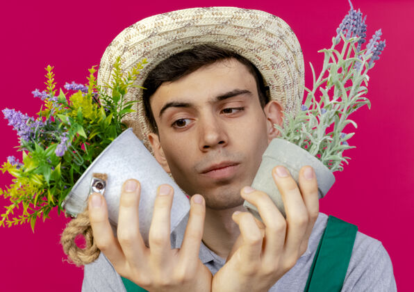 花园困惑的年轻男园丁戴着园艺帽 拿着花盆看园艺复制粉色