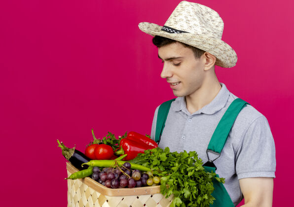 空间高兴的年轻男园丁戴着园艺帽 抱着菜篮看了看男性园艺请