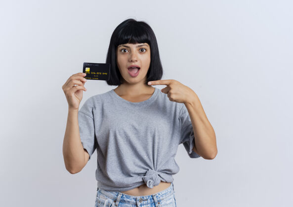 年轻兴奋的年轻黑发高加索女孩持有并指向信用卡空间举行信贷