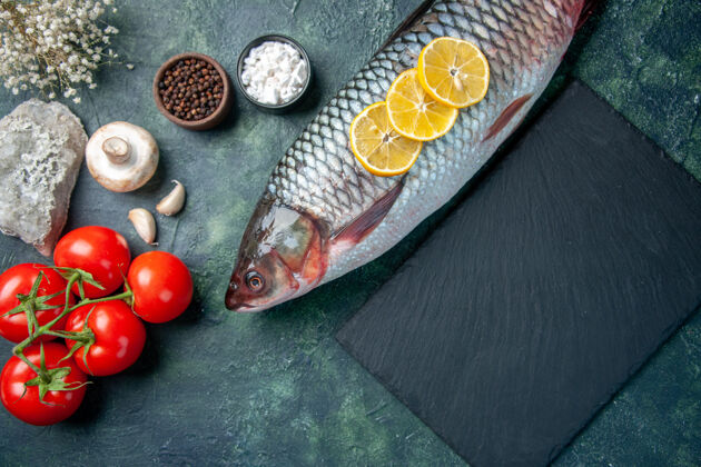深色在深蓝色的背景上俯瞰新鲜的生鱼片和西红柿风景晚餐海鲜
