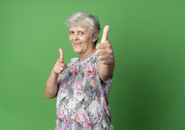 老人微笑的老妇人竖起大拇指 指着绿色的墙壁点老的绿的