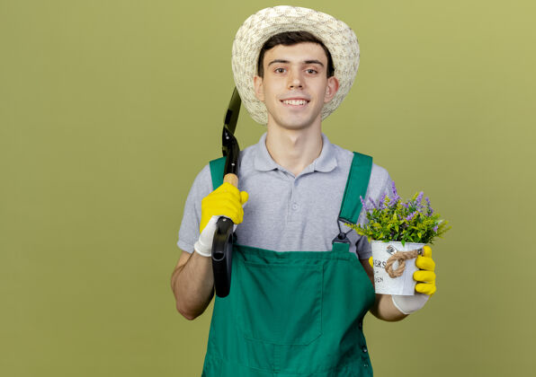 黑桃微笑的年轻男园丁戴着园艺帽和手套 手里拿着铁锹和花盆里的花复制园艺花