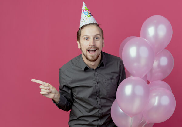 立场戴着生日帽的帅哥站在那里 氦气球指着旁边气球惊喜粉红色