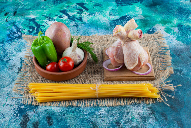 意大利面意大利面 一碗蔬菜 旁边的鼓槌放在一块麻布板上 背景是蓝色的胡椒新鲜蛋白质