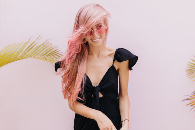 愉悦一个长着粉红色头发的女人站在工作室里奇异的棕榈树旁无忧无虑搞笑休息