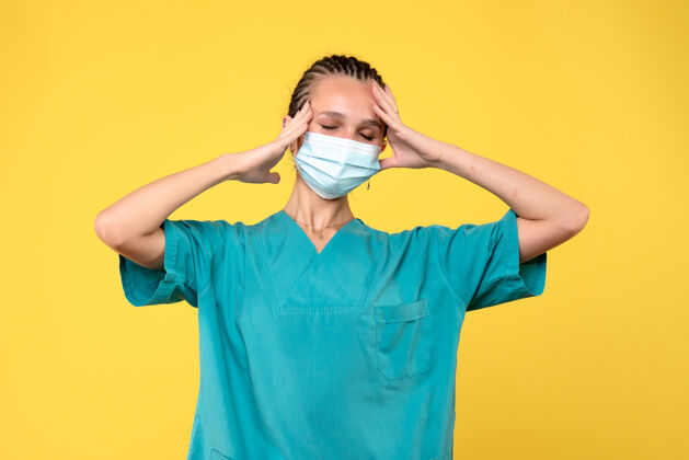 成人黄色墙壁上穿着医疗服 戴着无菌口罩的女医生的正视图面具医疗消毒