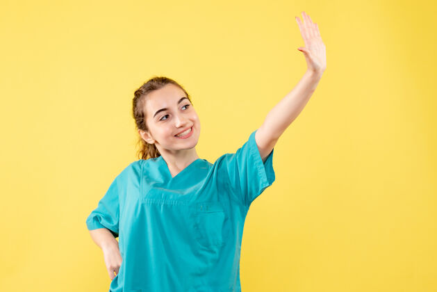 医疗身穿医用衬衫的年轻女医生在黄色墙壁上挥舞的正面视图衬衫病毒微笑