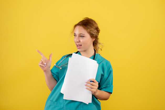 正面黄墙上穿着医疗服的女医生手持分析图手持病毒护士