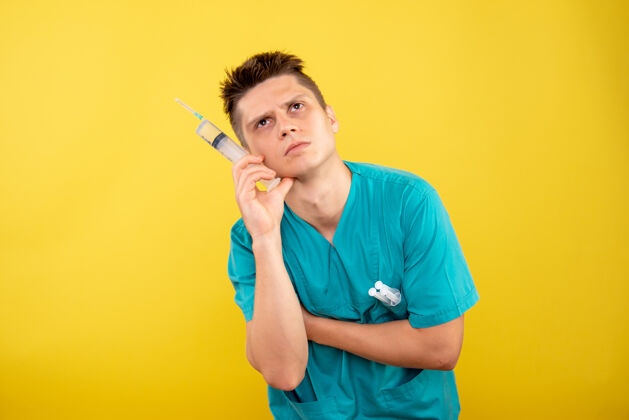 健康身穿医疗服的男医生手持针剂 在黄墙上思考男医生套装微笑