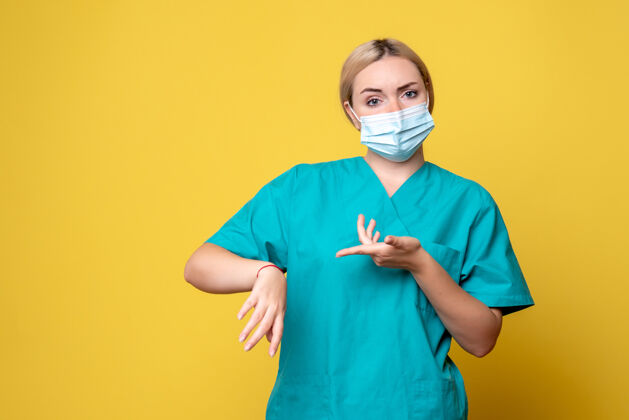 年轻女医生黄色墙上穿着医用衬衫和无菌口罩的年轻女医生的正视图男性男人面具