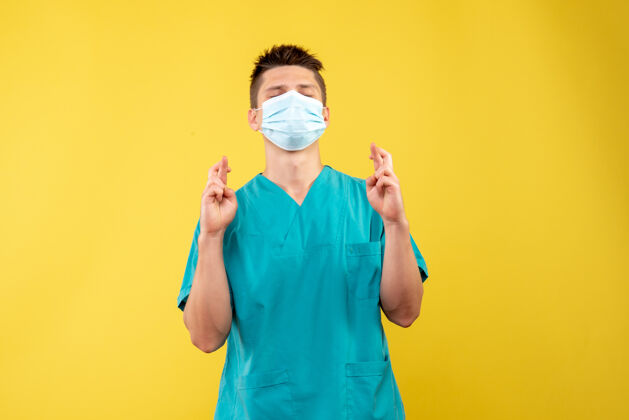 人身穿医疗服 戴着无菌口罩的男医生的正面图 希望在黄色的墙上人面具套装