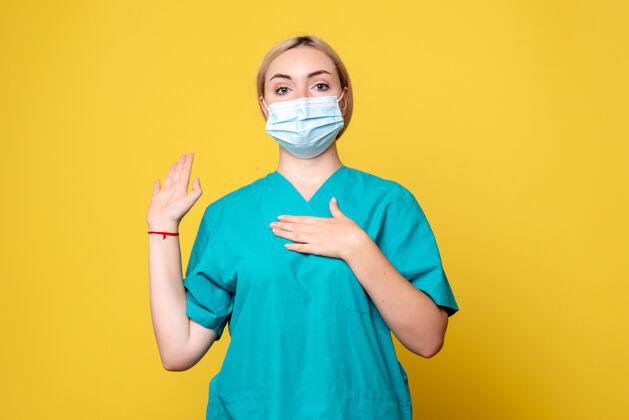 年轻女医生黄墙上年轻女医生穿着医用衬衫 戴着口罩的正面图流行病人脸