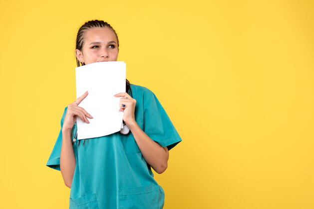 漂亮黄墙上穿着医疗服拿着纸的女医生的正视图微笑前面快乐