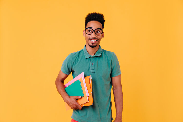 时尚穿着绿色t恤的有趣的非洲学生的肖像考试后戴眼镜拿着书和课本的幸福的黑人男孩的照片大学笔记本男人