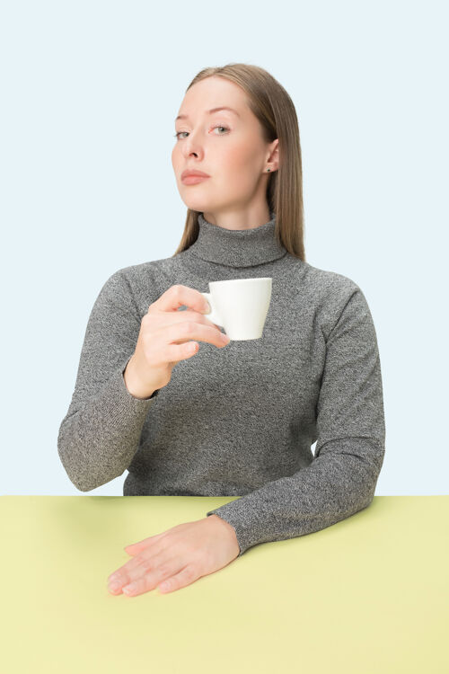 年轻美丽的孤独的女人坐在蓝色的工作室里 手里拿着一杯咖啡 看起来很悲伤茶沉思早餐