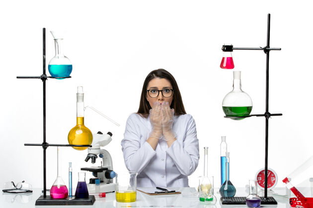 坐着前视图穿着白色医疗服的女化学家坐在白色背景上摆姿势实验室科学病毒柯维德大流行玻璃容器烧杯