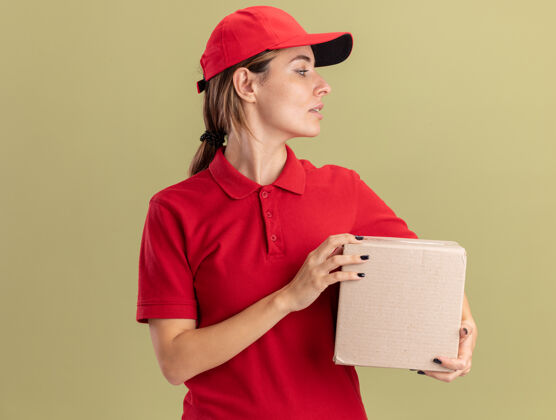 制服自信的年轻漂亮的女送货员穿着制服拿着名片盒 看着橄榄绿的一面姿势信心漂亮