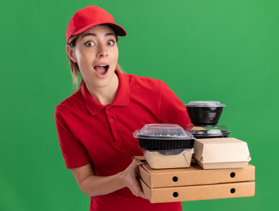 年轻人一个穿着制服的年轻漂亮的送货女孩拿着纸食品包装和容器在绿色的比萨饼盒上食物容器人