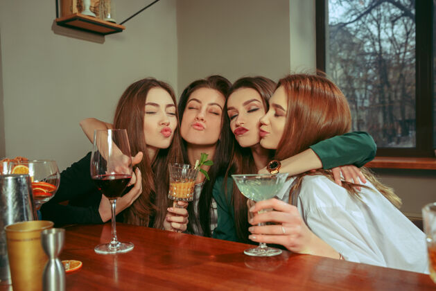 杯子女朋友在酒吧喝酒她们坐在一张摆着鸡尾酒的木桌旁她们穿着休闲服团体美丽手