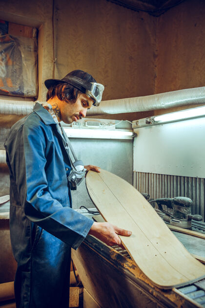 工作英俊的木匠在车间里用木溜冰鞋工作的肖像 剖面图电力工具木工