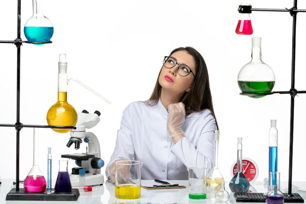 成人前视图穿着白色医疗服的女化学家坐在浅白背景上拿着解决方案科学大流行病毒冠状病毒实验室病毒前面西装