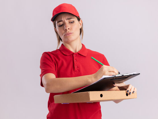 制服穿着制服的严肃年轻漂亮的送货女孩拿着笔和剪贴板在白色的比萨饼盒上成人比萨饼快递