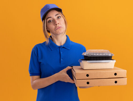 姿势令人印象深刻的年轻漂亮的女送货员在制服举行纸食品包装和比萨饼盒上的橙色容器印象盒子年轻