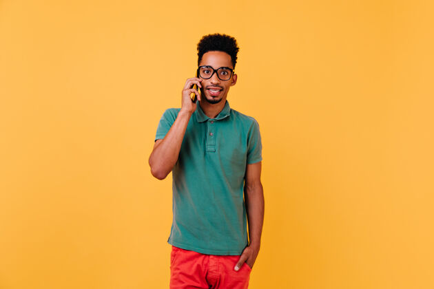 年轻惊讶的黑人男模在讲电话时髦的非洲男人戴着眼镜和智能手机合影手机男人乐趣
