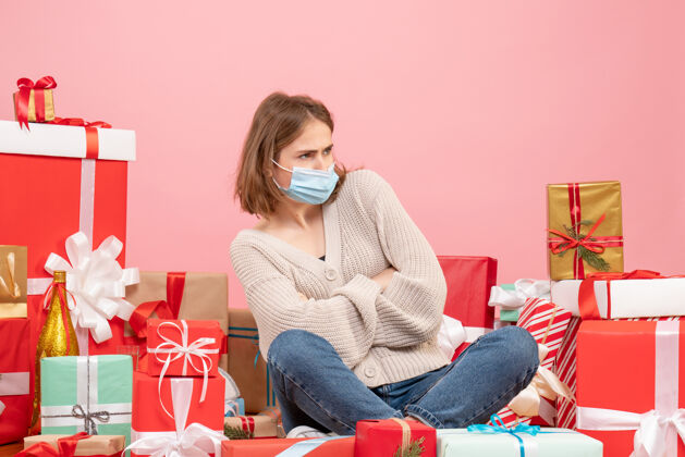 情绪正面图：坐在圣诞节周围的年轻女性戴着无菌面具出现面具电脑消毒