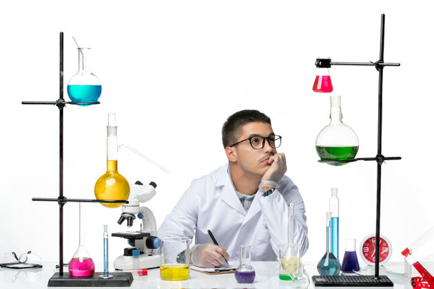 医学正面图：穿着医学套装的男性化学家坐在白色背景上写着什么病毒冠状病毒飞溅疾病科学烧杯写作前面