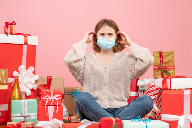 年份正面图：坐在圣诞节周围的年轻女性戴着无菌面具出现坐着圣诞节病毒