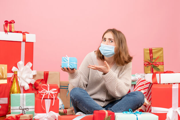 情绪正面图：坐在圣诞节周围的年轻女性戴着无菌面具出现面具粉色礼物