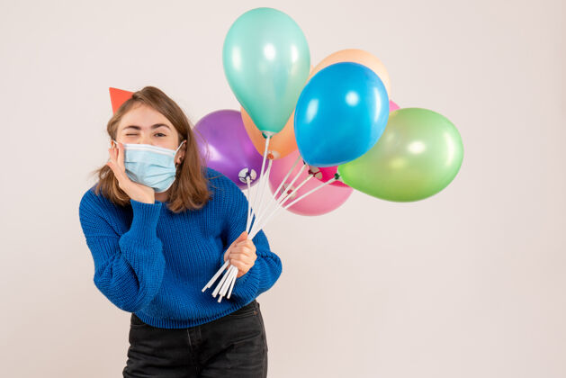 面具正面图：戴着消毒面具的年轻女性手持五颜六色的气球聚会气球庆祝