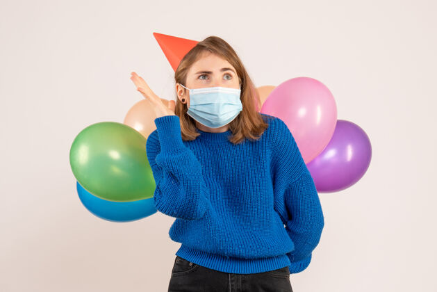五颜六色正面图：戴着无菌口罩的年轻女性把五颜六色的气球藏在背后乐趣气球生日