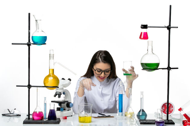 实验室正面图：穿着白色医疗服的女化学家拿着白色桌子上的装有溶液的烧瓶科学病毒冠状病毒-大流行实验室容器正面烧瓶