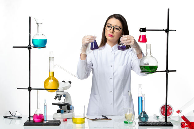 视图正面图：穿着无菌医疗服的女化学家拿着装有紫色溶液的烧瓶 背景是白色的病毒疾病冠状病毒-大流行科学成人科学实验室