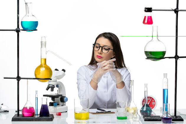 医学前视图穿着白色医疗服的女化学家坐在白色背景的不同的解决方案上科学大流行病毒冠状病毒实验室坐着前面微笑